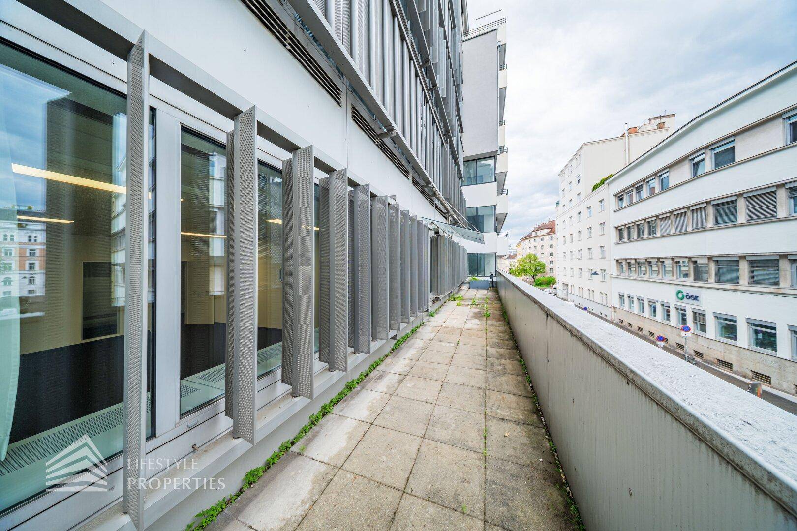 Schmale Außenterrasse mit Steinplatten und einem Blick auf die angrenzenden Gebäude und die Straße.