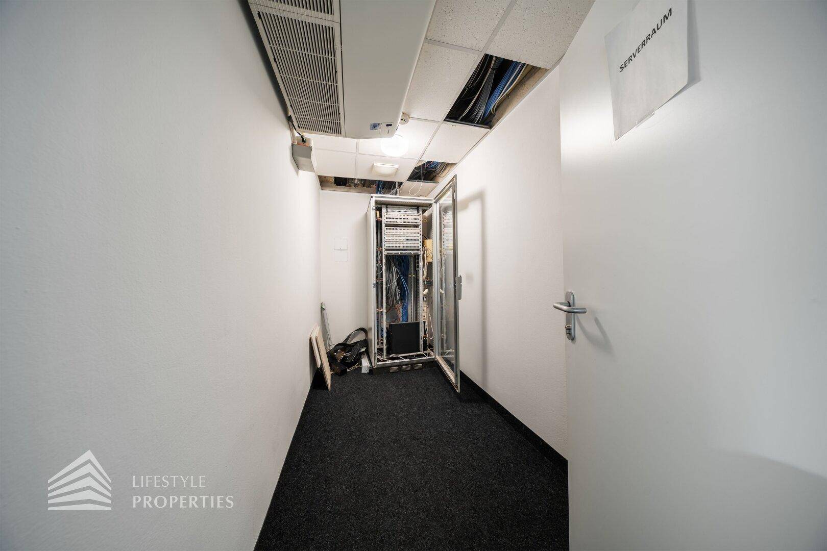 Serverraum mit offener Deckenkonstruktion und sichtbaren Kabeln, ausgestattet mit einem Serverschrank.