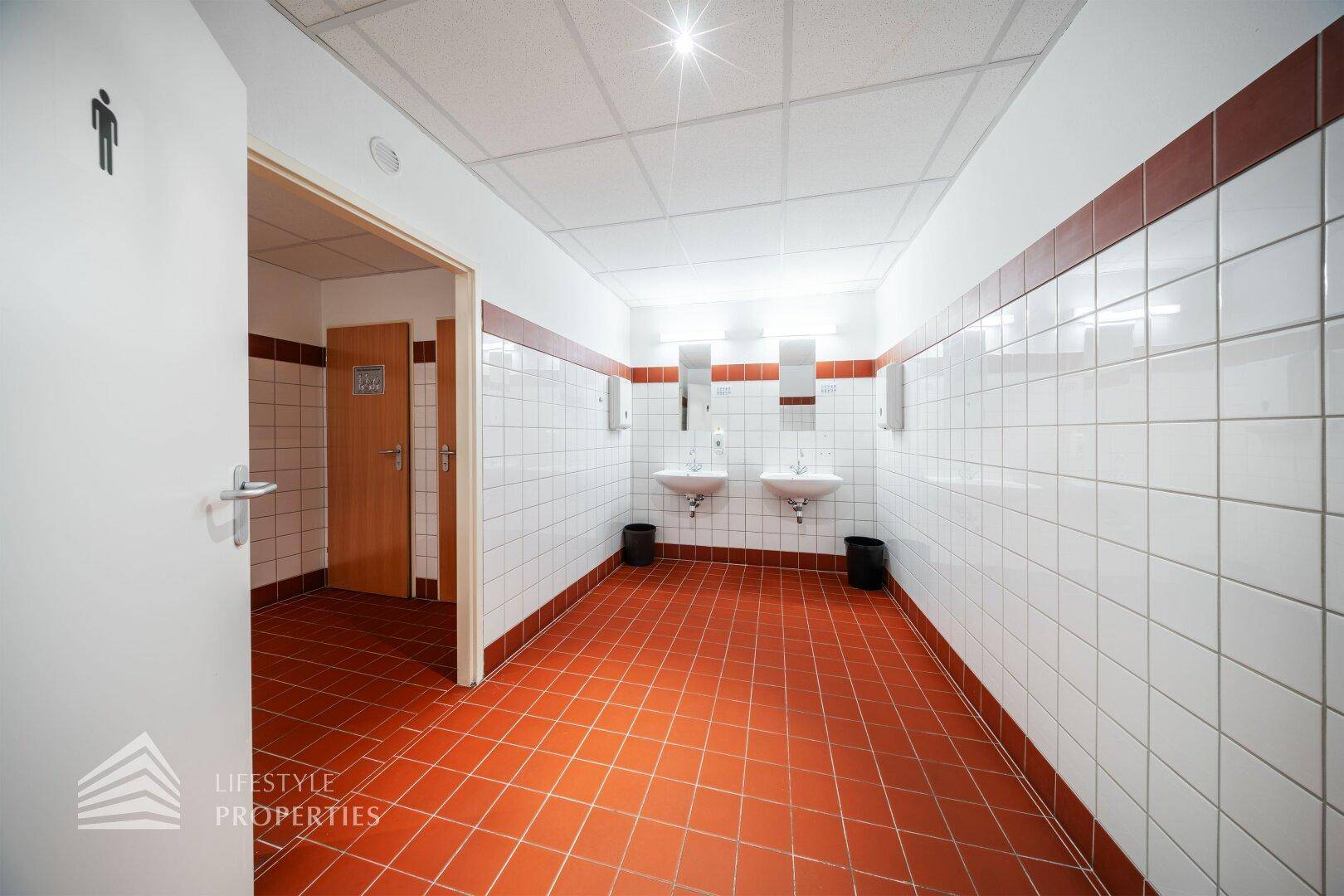 Geräumiger Sanitärbereich mit roten Bodenfliesen und weißen Wandfliesen, ausgestattet mit zwei Waschbecken.