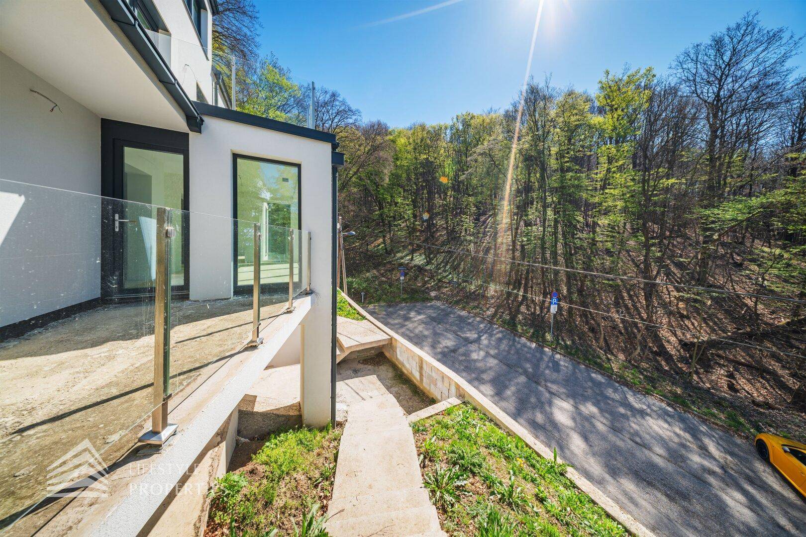 Außenbereich der Villa mit Treppen und Glasgeländer, umgeben von Bäumen und Natur.