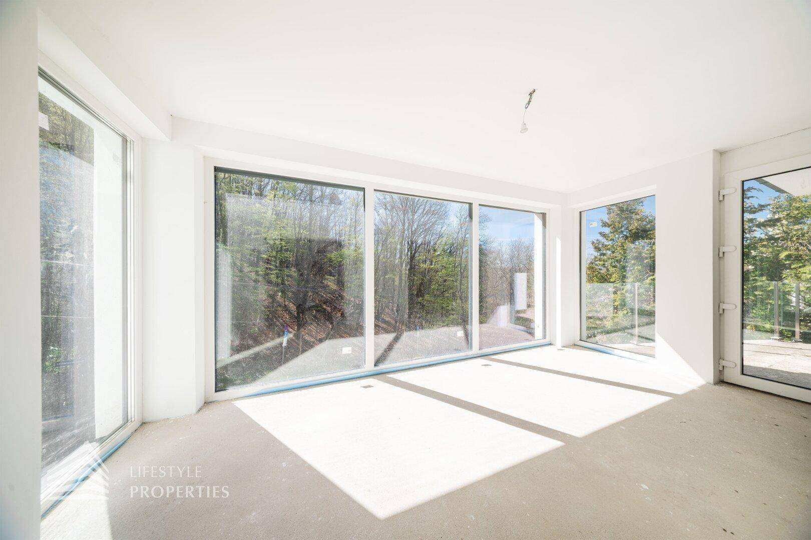 Heller, unmöblierter Raum im Rohbau mit großen Fensterfronten und viel Tageslicht.