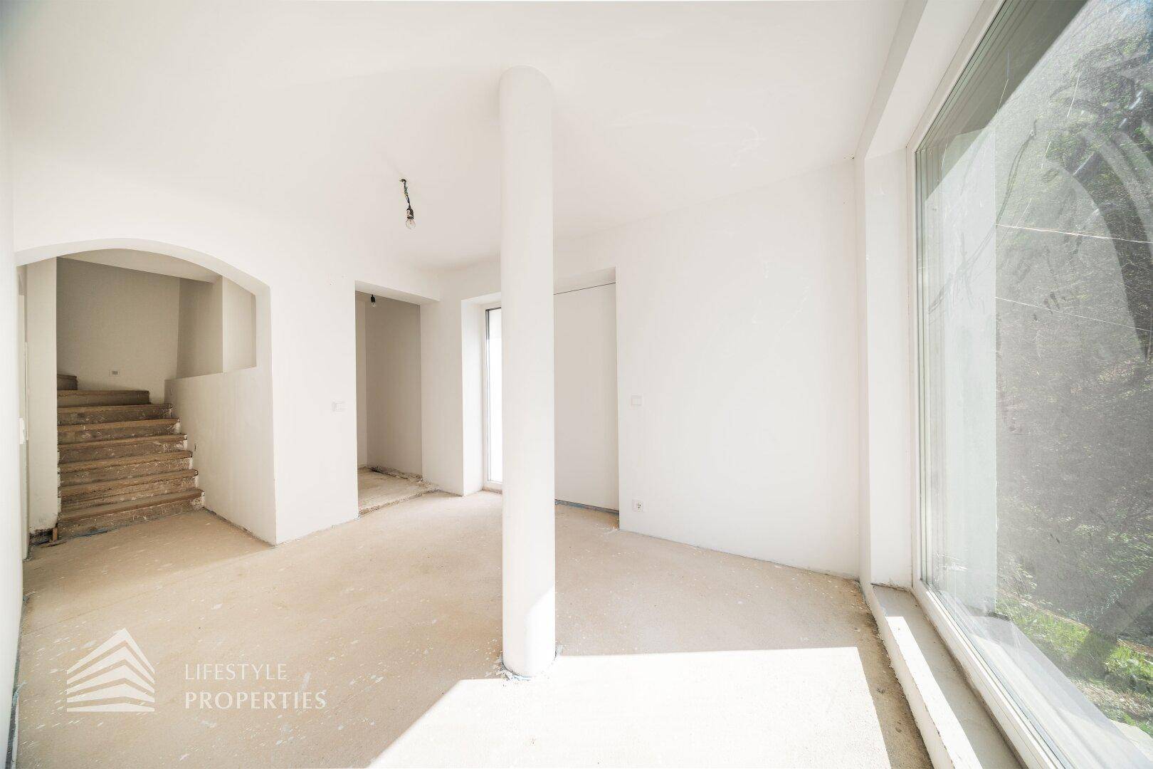 Heller Eingangsbereich im Rohbau mit Treppenaufgang und großem Fenster für natürliches Licht.