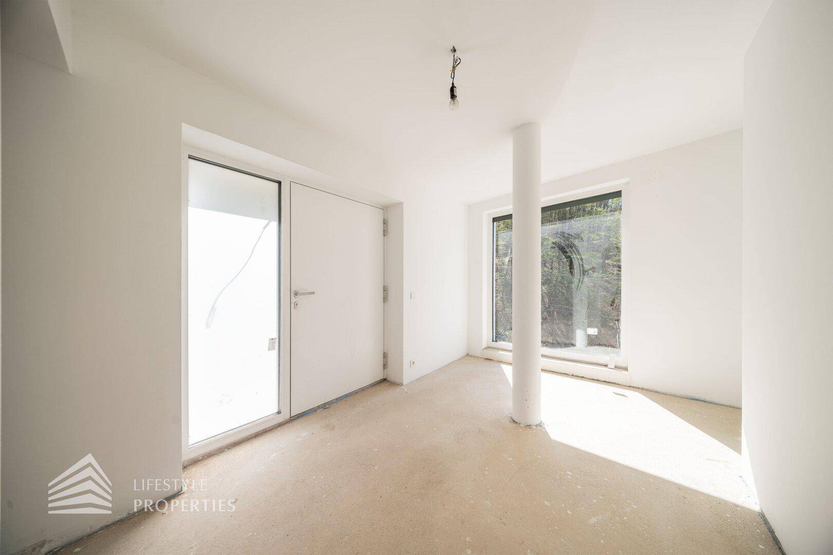 Unmöblierter Raum im Rohbau mit Tür und Fenster, ideal für einen Empfangsbereich oder Flur.