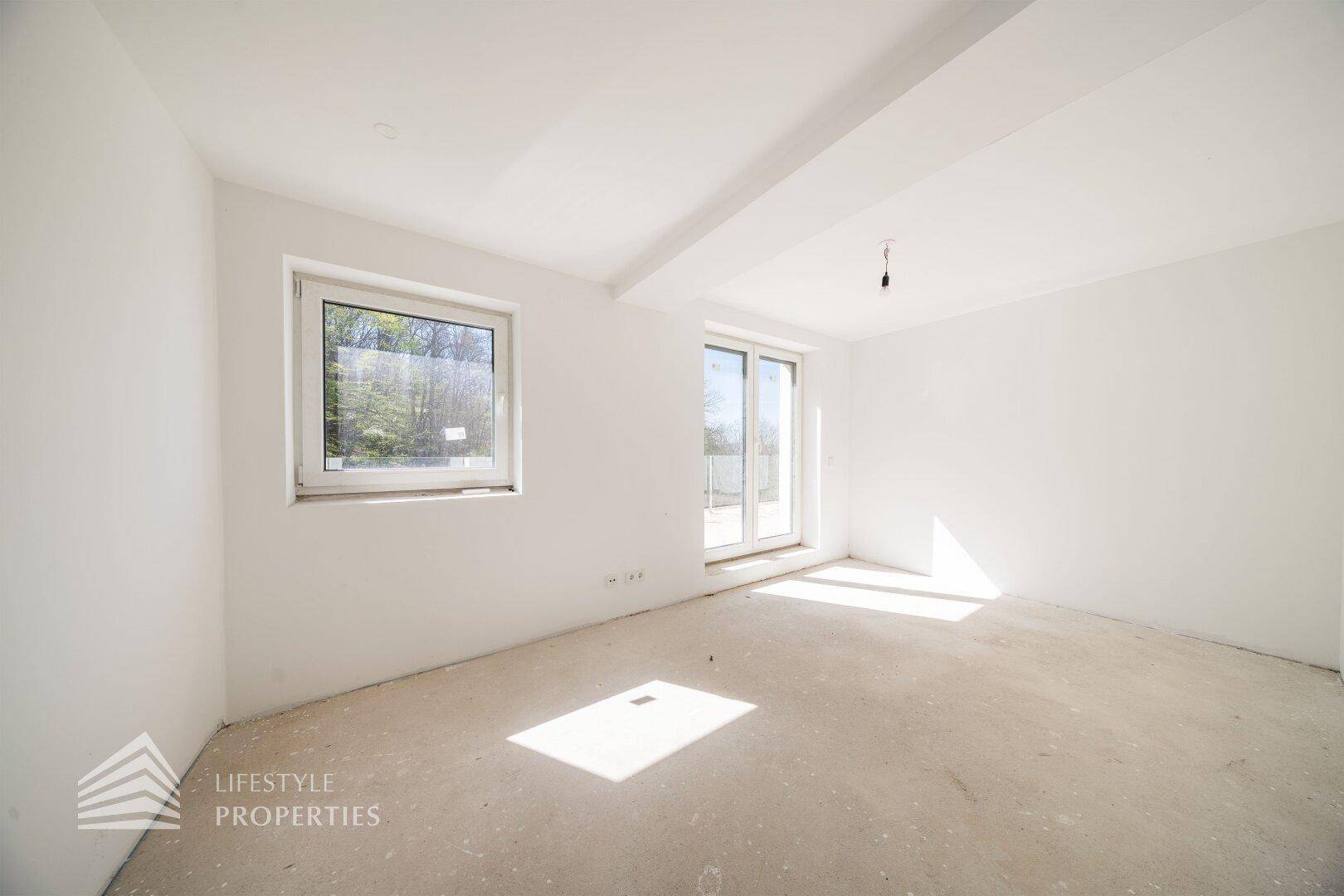 Heller Raum im Rohbau mit Fenster und Zugang zu einem möglichen Balkon, ideal als Schlafzimmer.