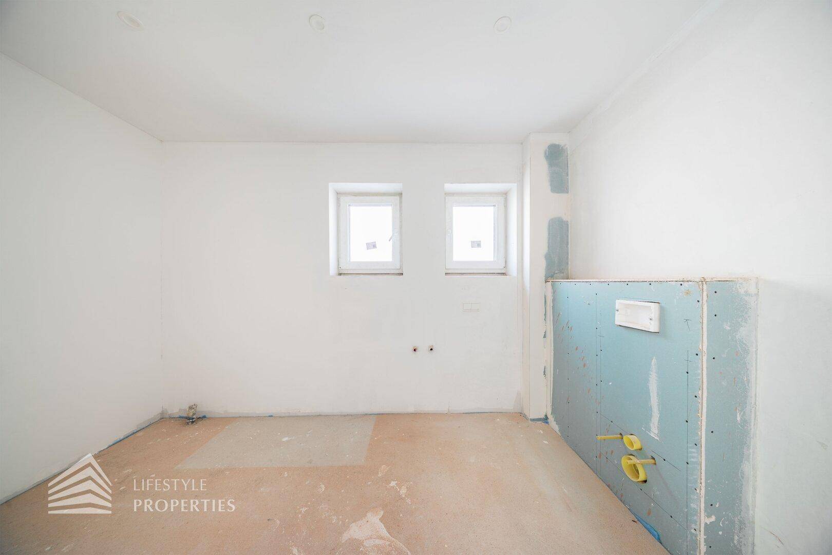 Badezimmer im Rohbau mit vorbereiteten Anschlüssen und kleinen Fenstern für die Belüftung.