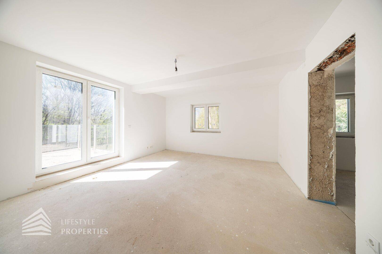 Geräumiger Raum im Rohbau mit großen Fenstern und viel Tageslicht, bereit zur Fertigstellung.