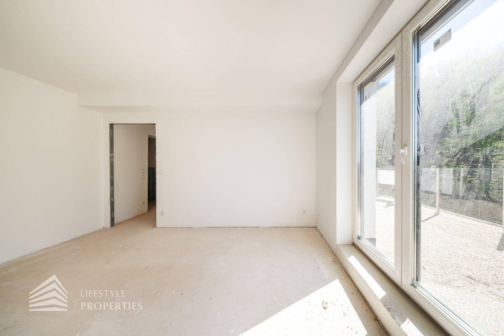 Heller Raum im Rohbau mit Fensterfront und Zugang zu einem Außenbereich, ideal für Wohnzwecke.