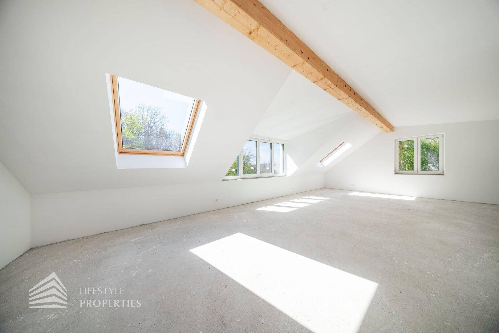 Lichtdurchfluteter Dachbodenraum im Rohbau mit mehreren Dachfenstern und Holzbalken.