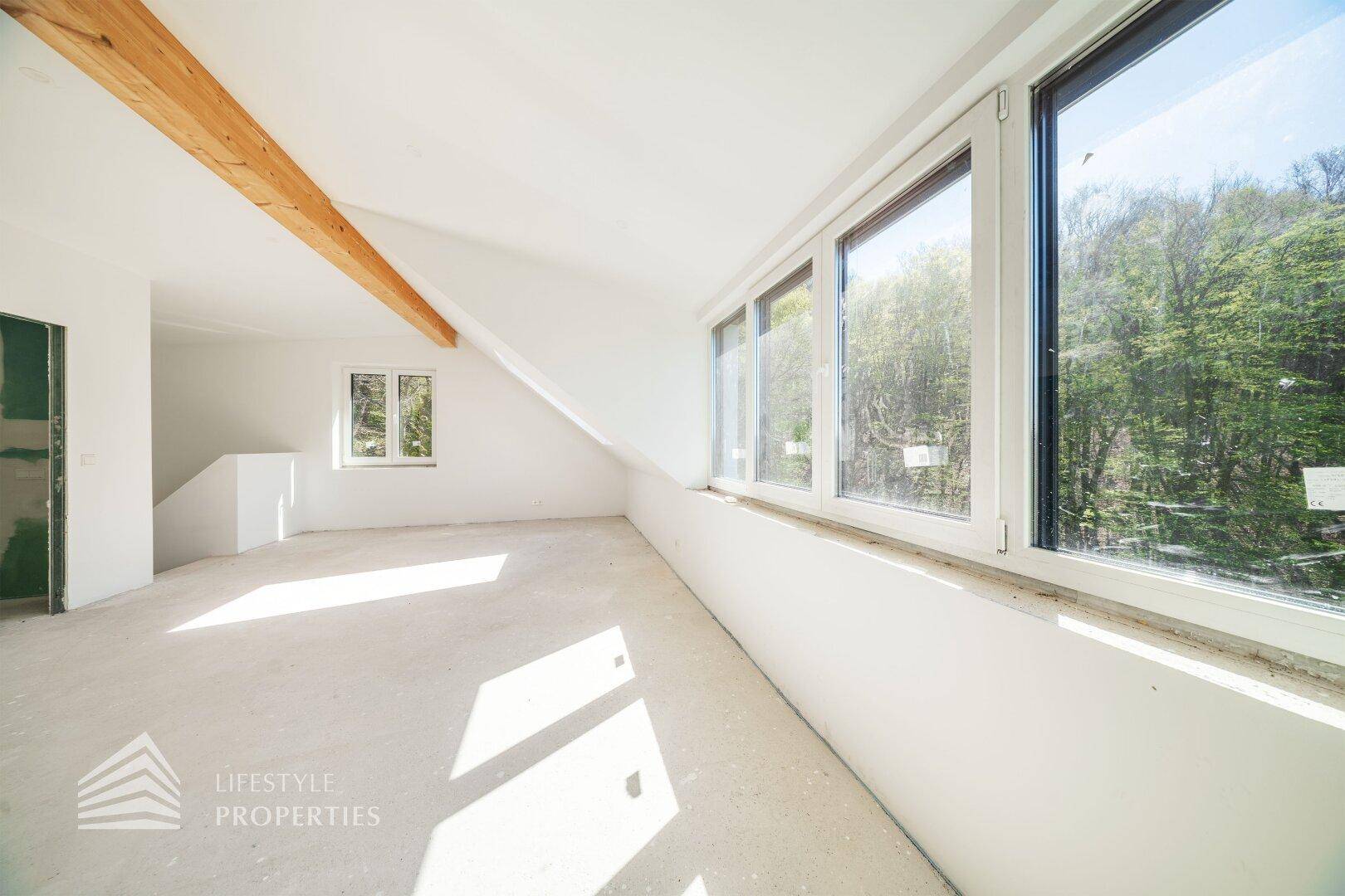 Heller Dachbodenraum im Rohbau mit sichtbarem Holzbalken und Fenstern für natürliches Licht.