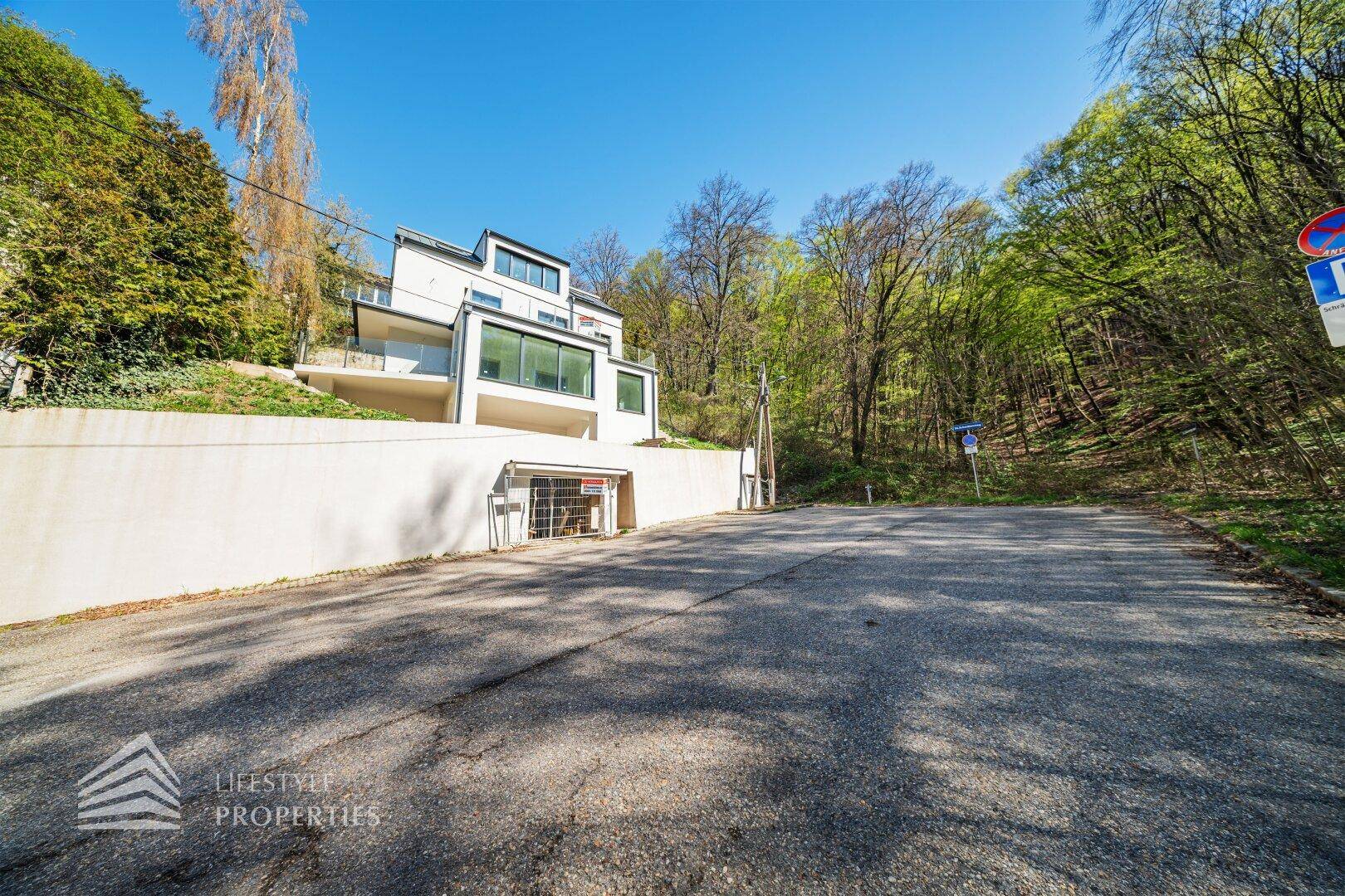 Moderne Villa am Hang mit Tiefgaragenzufahrt und umgebender Natur.