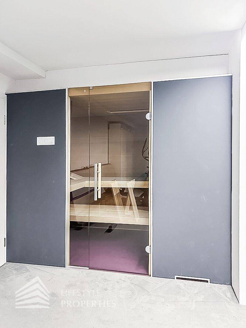 Moderne Sauna mit Glasfront, Holzbänken und Zugang zum Fitnessbereich.
