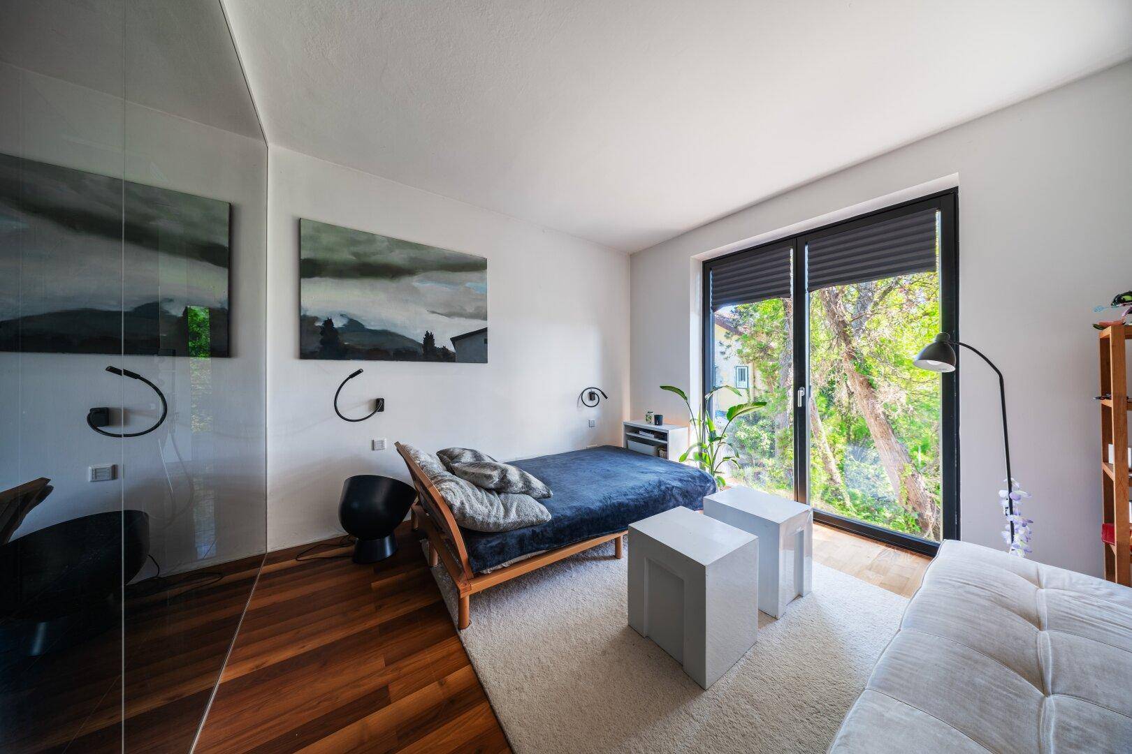 Helles Schlafzimmer mit Holzboden, großem Fenster und modernem Bettgestell.