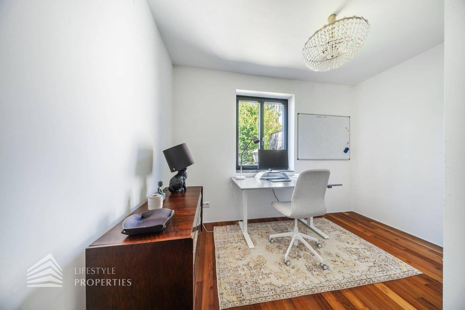 Helles Arbeitszimmer mit Holzboden, Schreibtisch und Fensterblick ins Grüne.