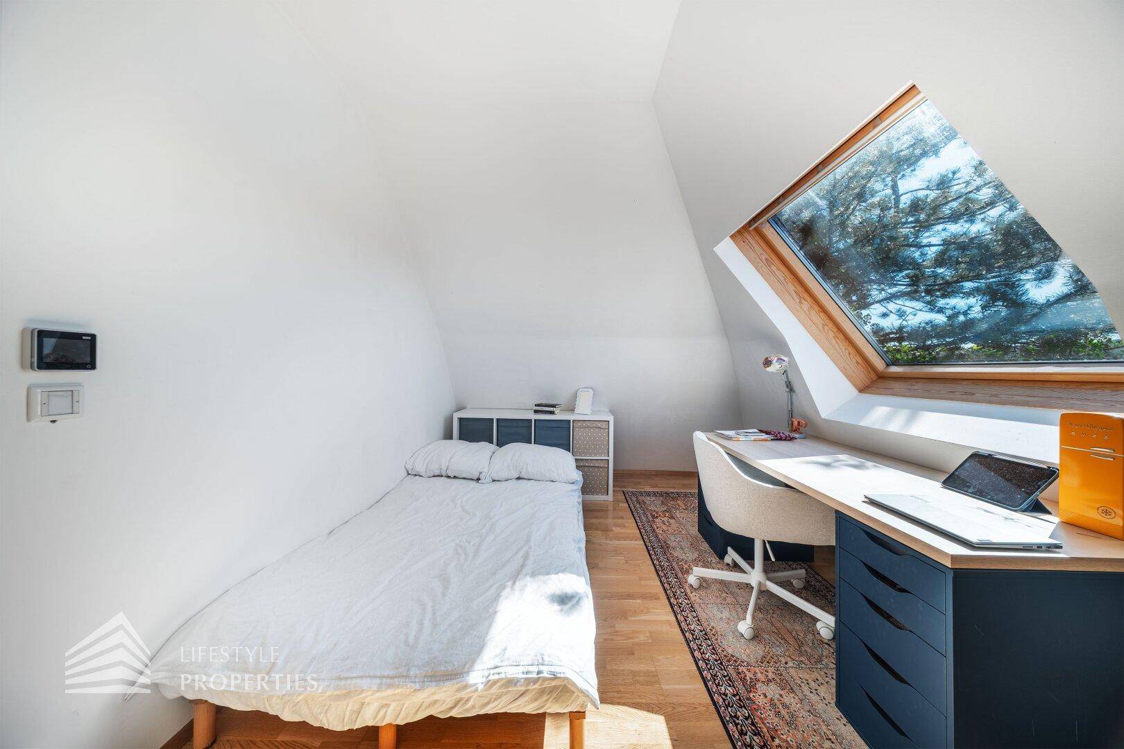 Helles Schlafzimmer im Dachgeschoss mit Einzelbett, Schreibtisch und großem Dachfenster.
