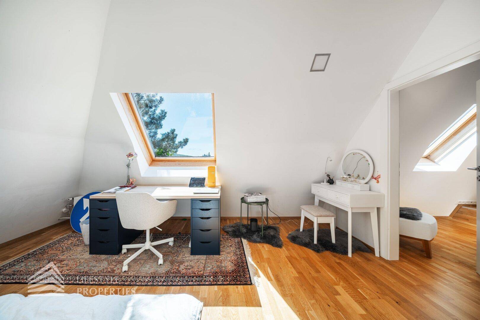 Helles Arbeitszimmer im Dachgeschoss mit Schreibtisch, Dachfenster und Holzboden.