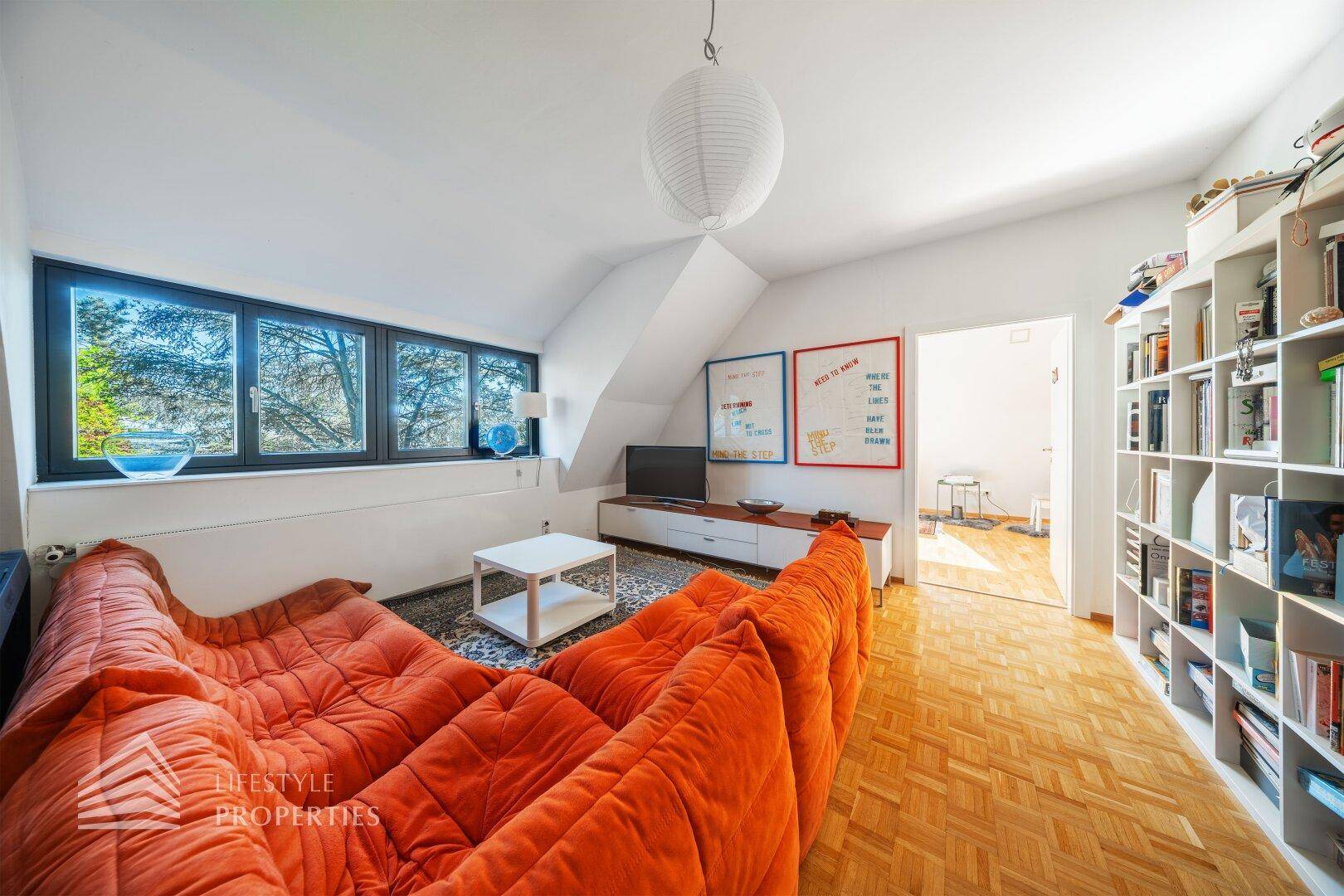 Gemütliches Wohnzimmer im Dachgeschoss mit orangefarbenem Sofa und Parkettboden.