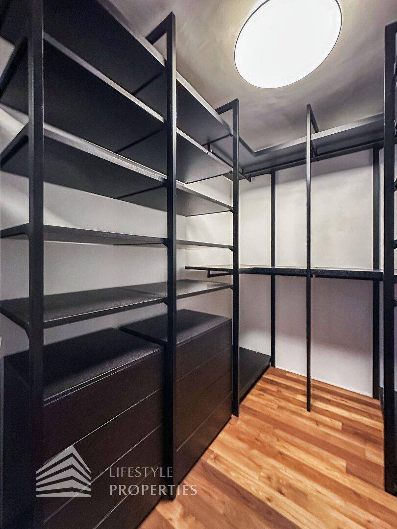 Geräumiger begehbarer Kleiderschrank mit dunklen Regalen und Holzboden.