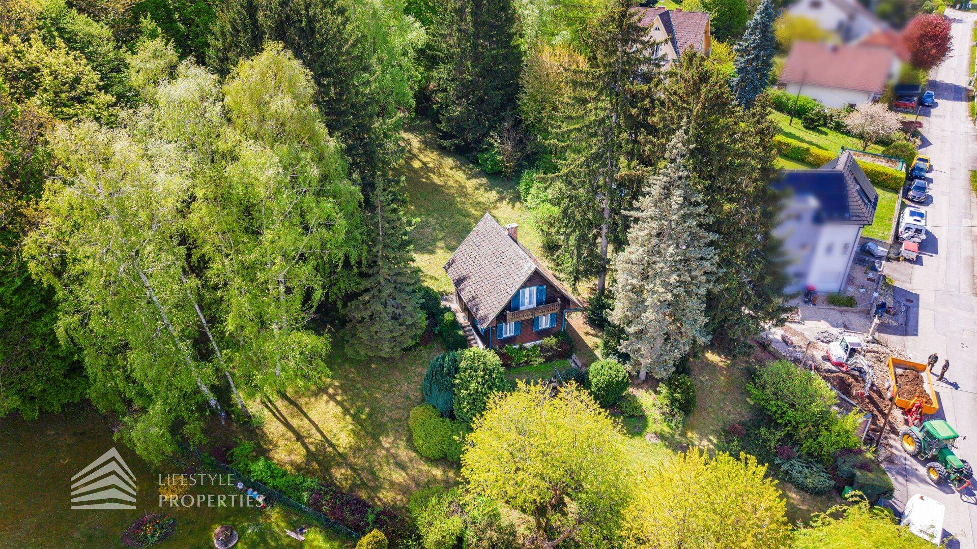 Blick von oben auf das Holzhaus mit seinem grünen Garten und der umliegenden Wohngegend.