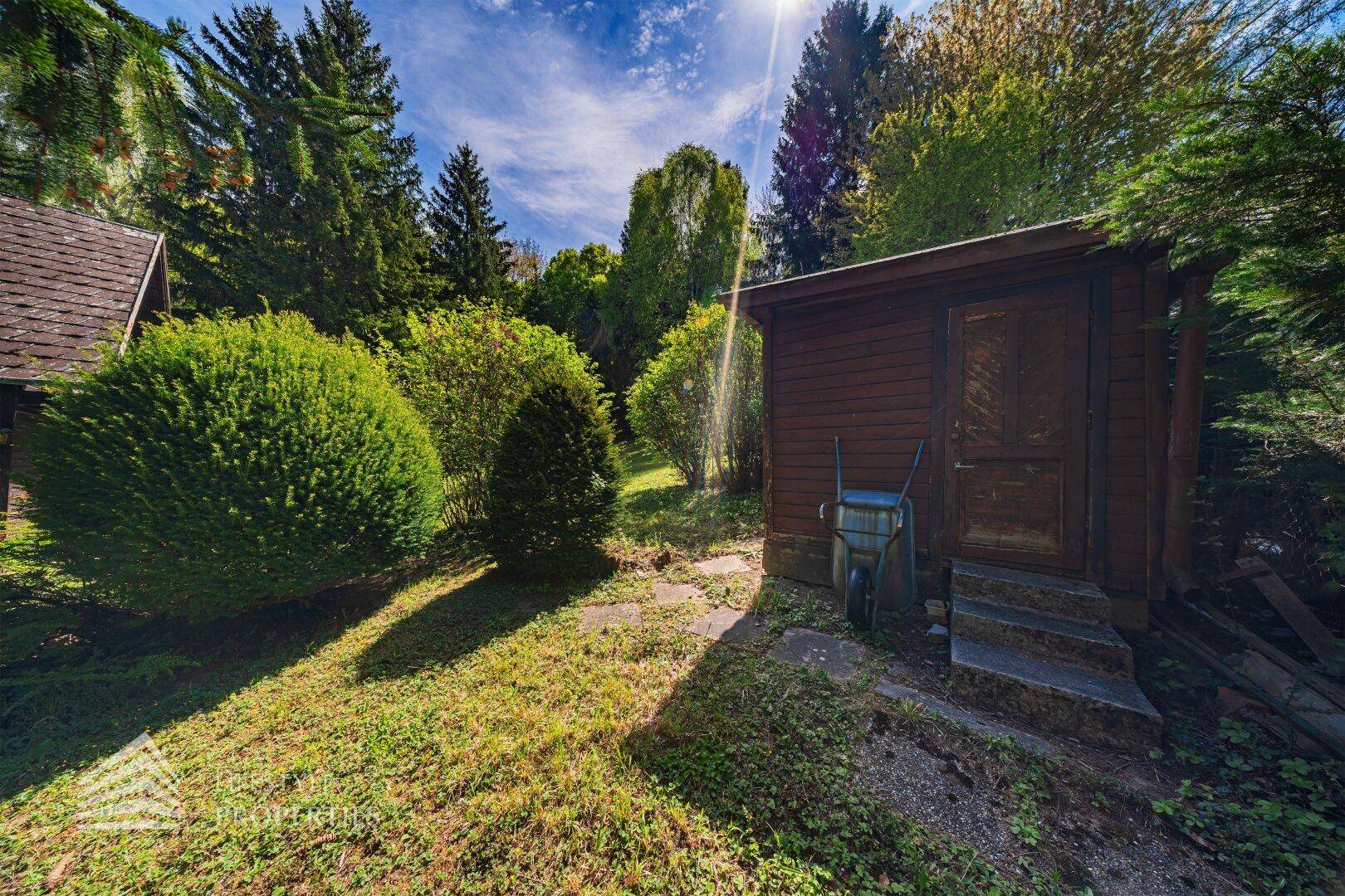 Praktischer Holzschuppen im Garten, umgeben von Grün und Bäumen, ideal für Gartengeräte.
