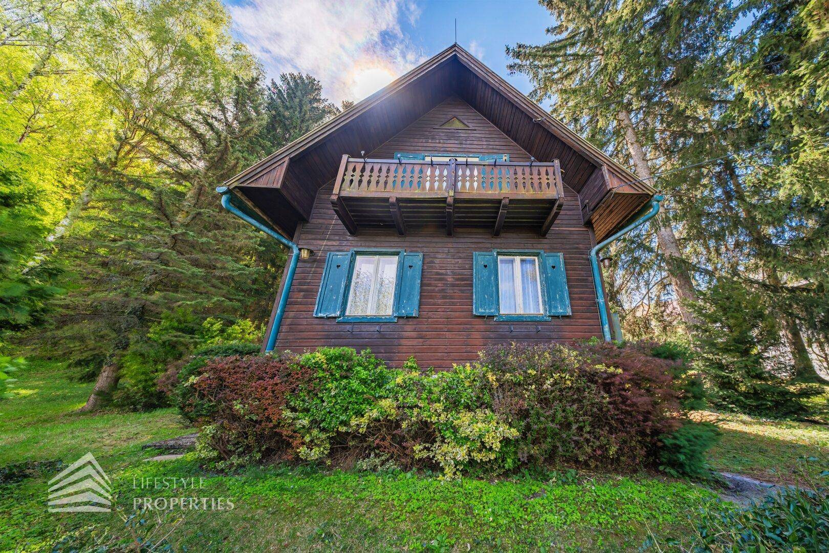 Vorderansicht des Holzhauses mit Balkon im Obergeschoss und grünen Fensterläden.