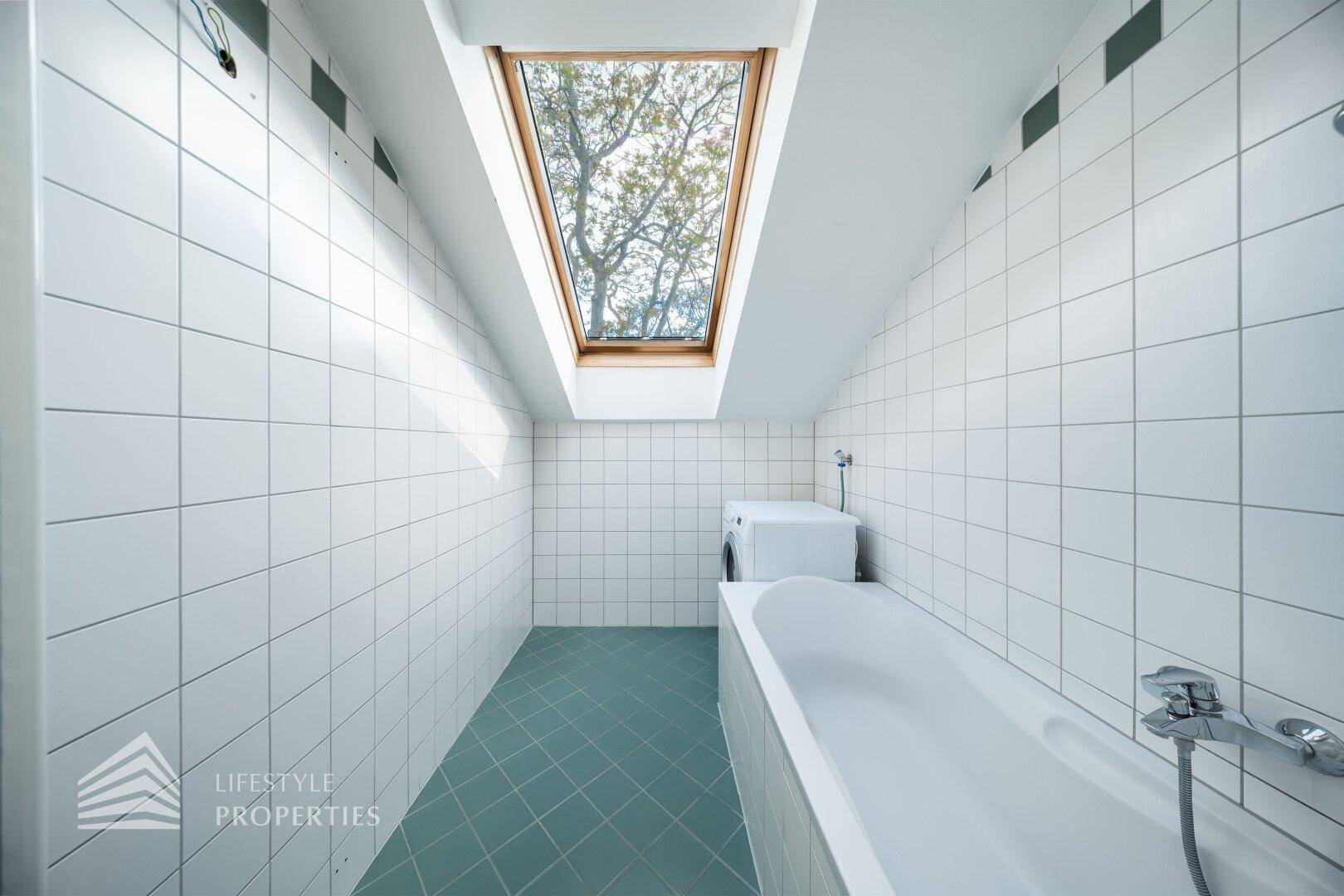 Badezimmer mit Badewanne, Waschmaschine, weißen Wandfliesen und Dachfenster.