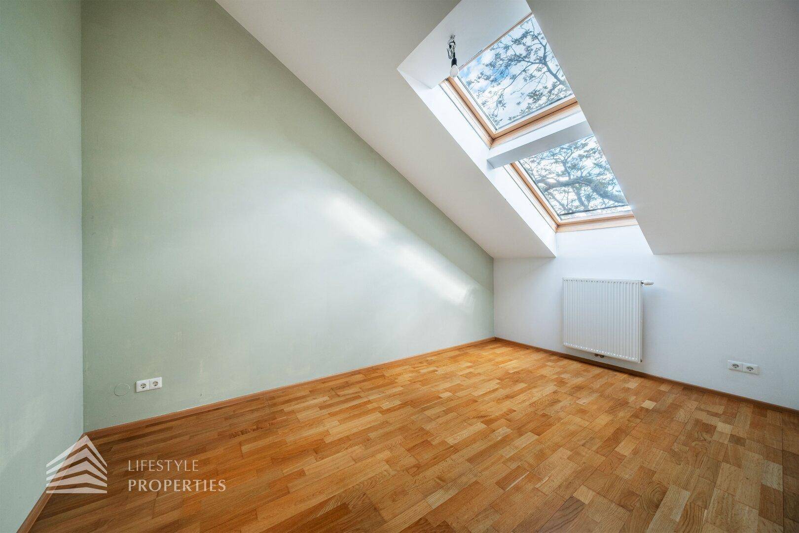 Gemütliches Schlafzimmer im Dachgeschoss mit Parkettboden, grüner Akzentwand und Dachfenstern.