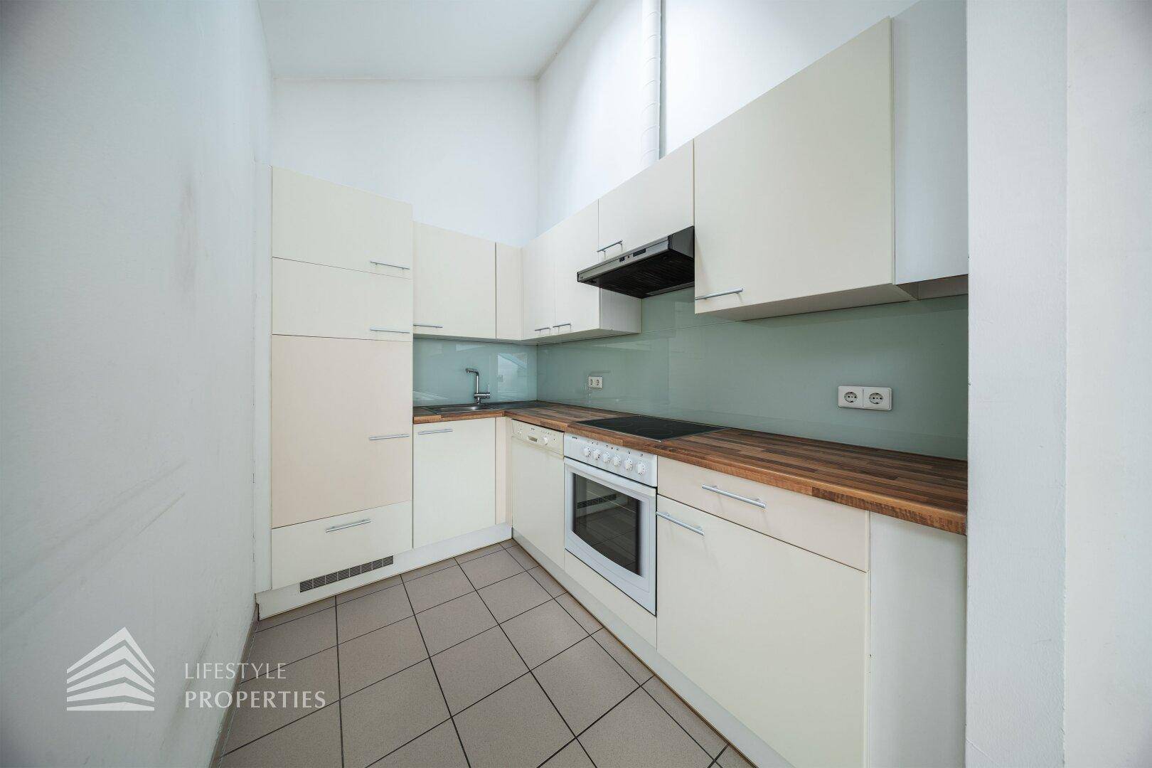 Kleine, funktionale Küche mit hellen Einbauschränken, Holz-Arbeitsplatte und Fliesenboden.