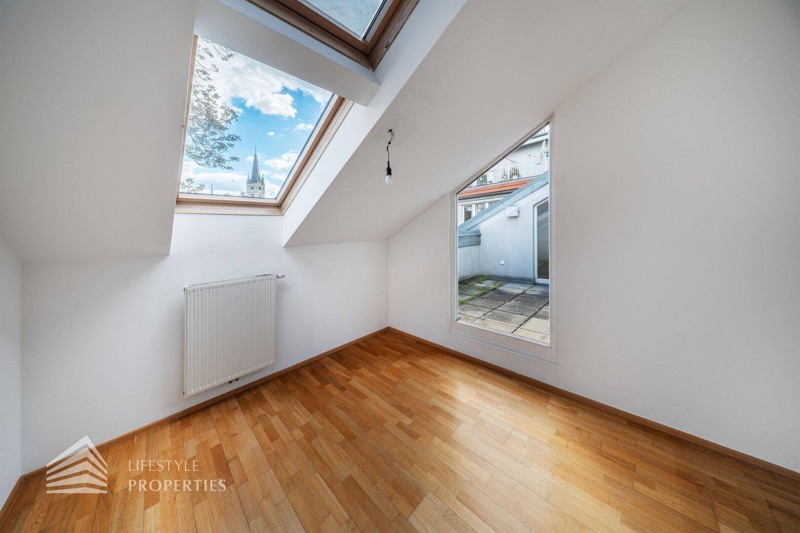 Schlafzimmer mit Parkettboden, Dachfenster und einem kleinen Fenster mit Blick auf die Terrasse.