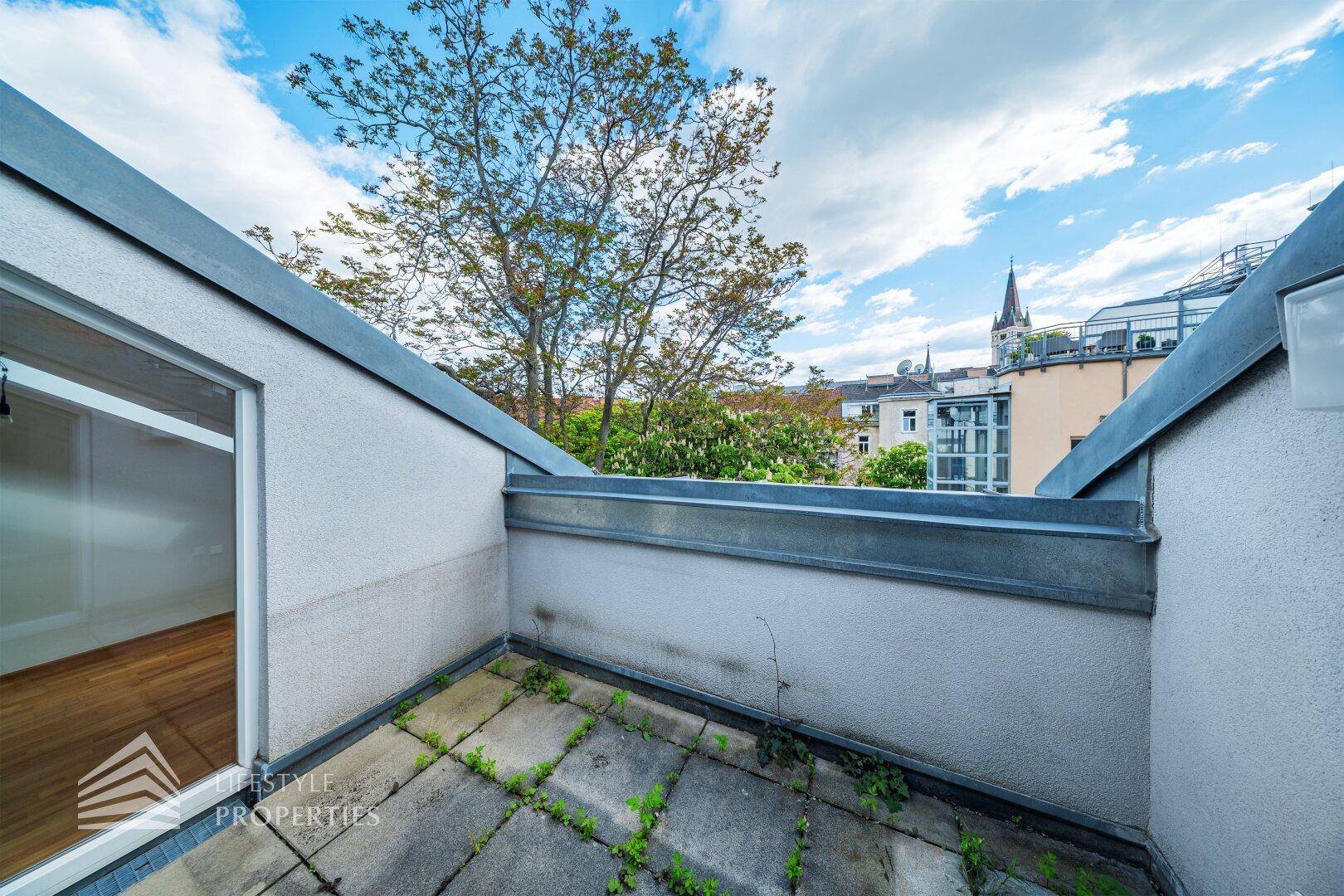 Kleine Dachterrasse mit Steinplatten und Blick auf die umliegenden Gebäude und einen Kirchturm.