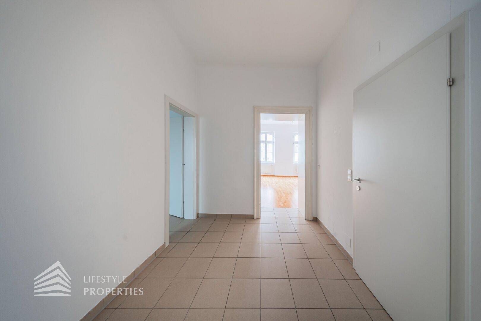 Heller Flur mit Fliesenboden und Zugang zu mehreren Zimmern, inklusive Blick in einen Wohnraum.