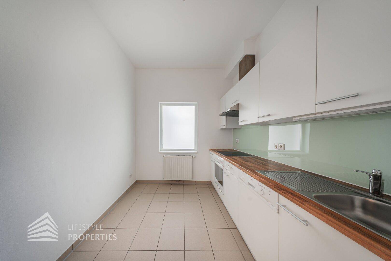 Helle Küche mit weißer Einrichtung, Holz-Arbeitsplatte und Fenster für Tageslicht.
