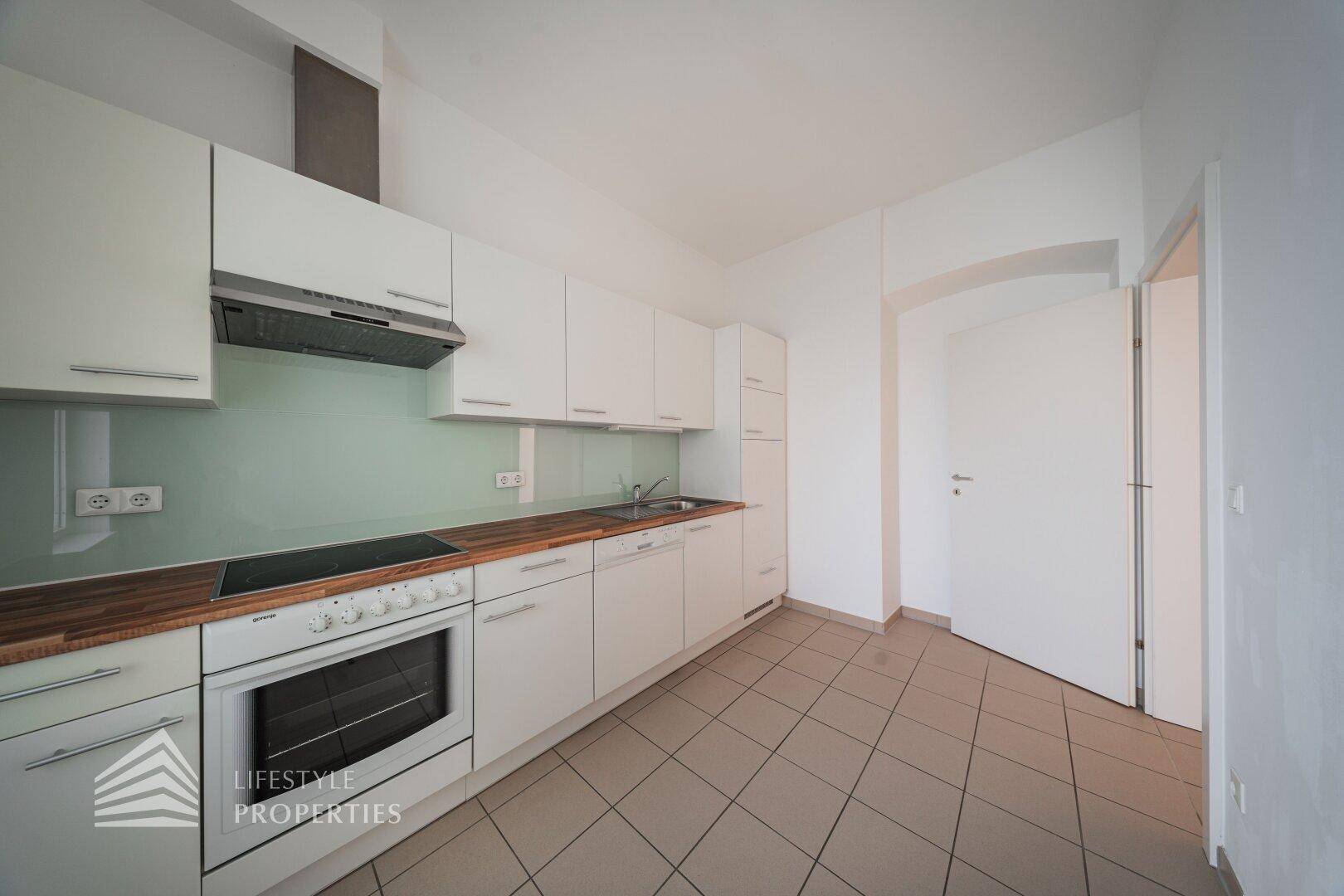 Moderne Einbauküche mit weißen Schränken, Holz-Arbeitsplatte und Fliesenboden.