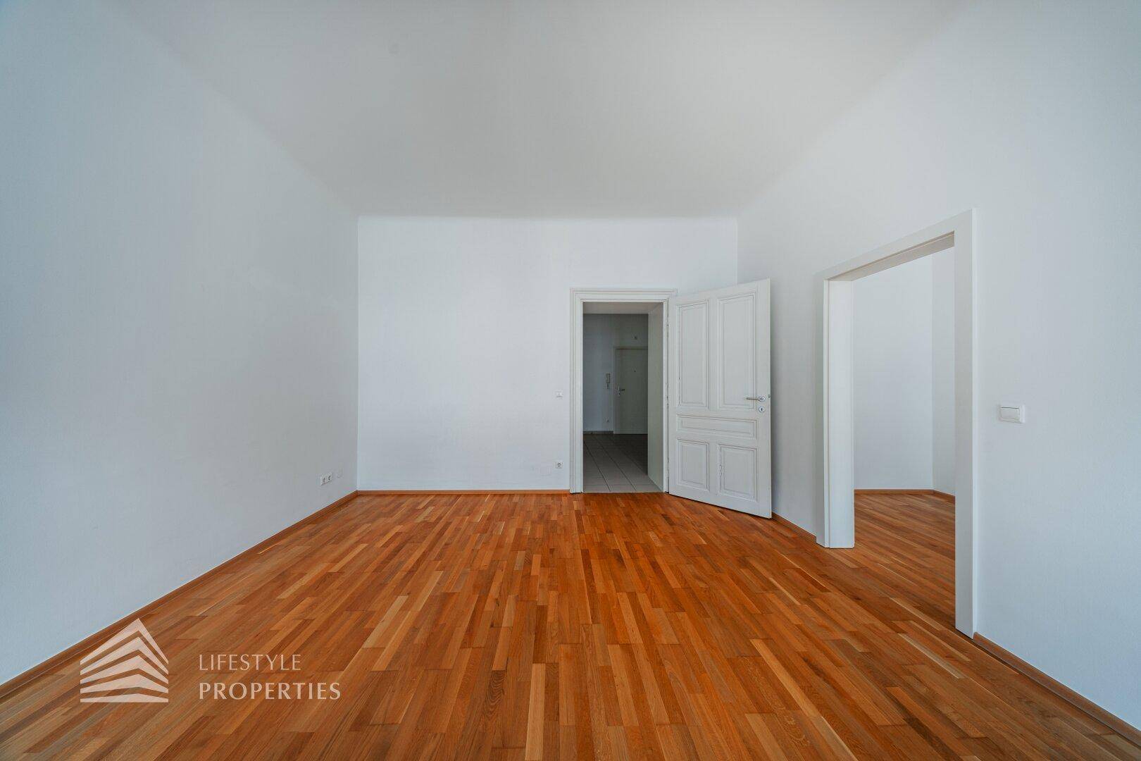 Leeres Zimmer mit klassischem Parkettboden und weißen Wänden, bietet vielseitige Nutzungsmöglichkeiten.