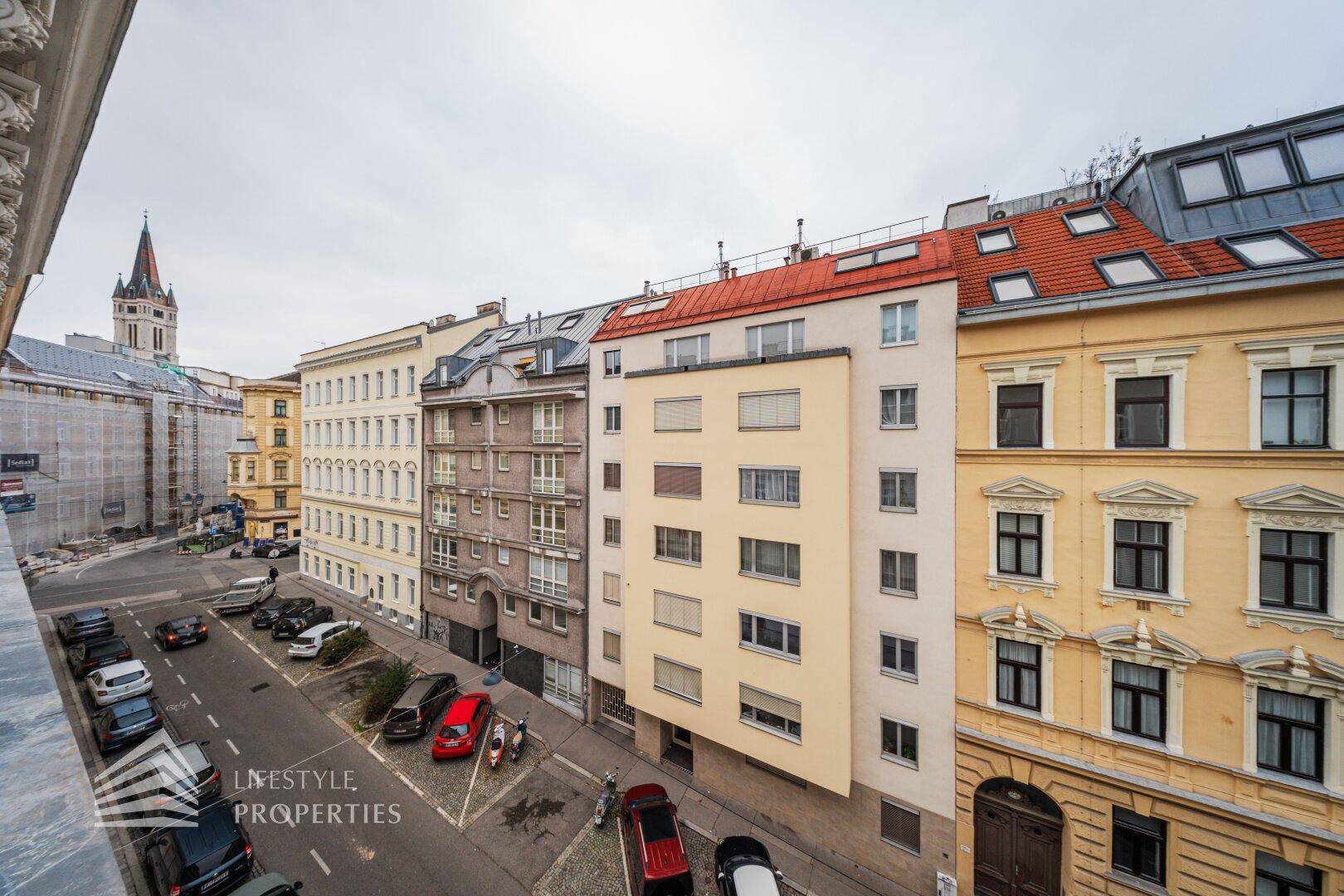 Blick von oben auf eine belebte Stadtstraße mit parkenden Autos und umliegenden Gebäuden.