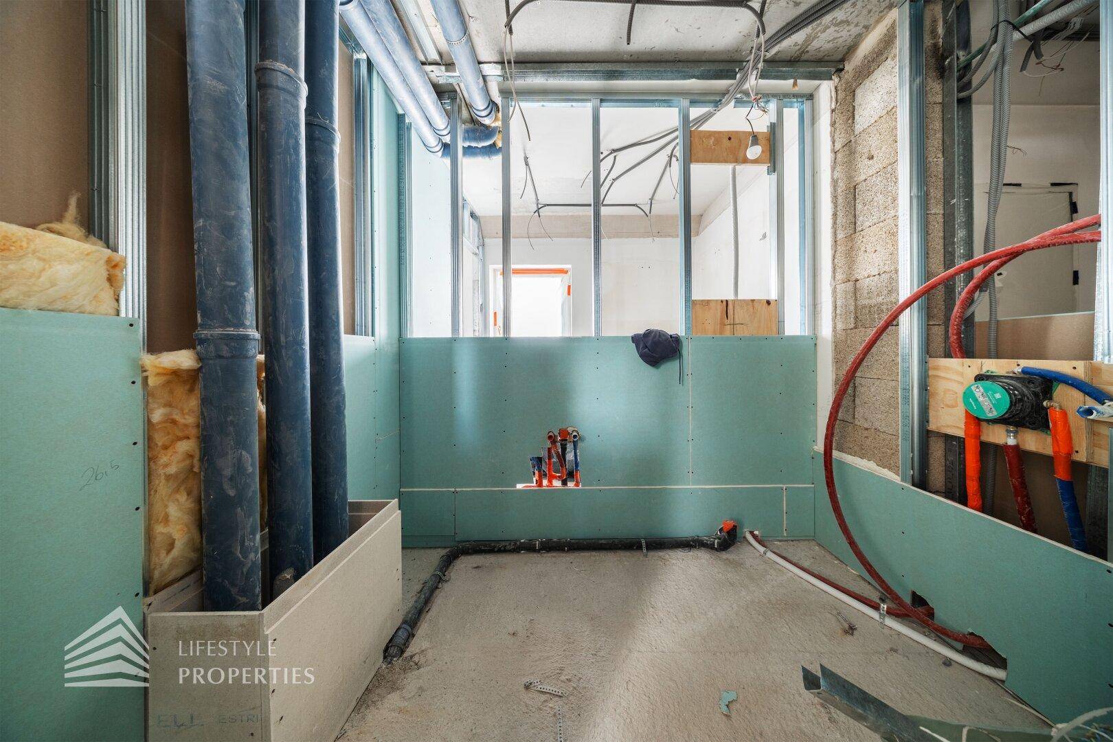 Raum im Rohbau mit sichtbaren Sanitärinstallationen und Trockenbauwänden.