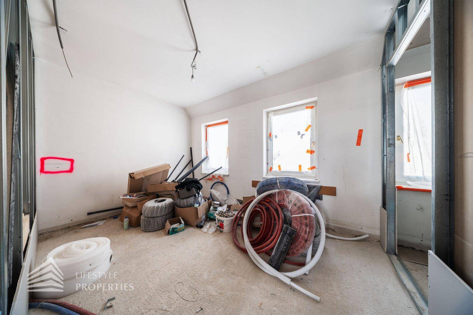 Raum im Rohbau mit Fenstern und Baumaterialien, bereit für den Ausbau.