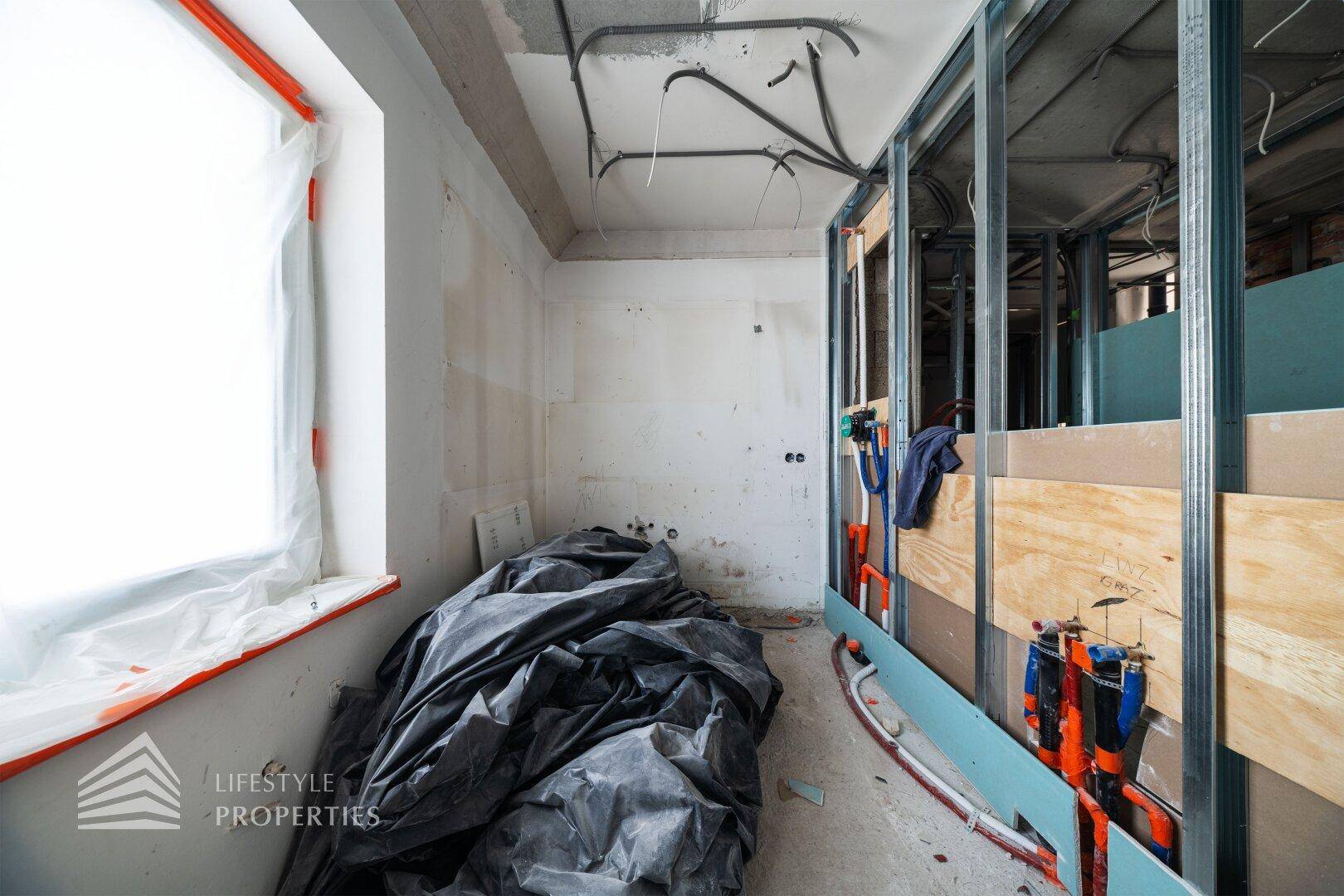 Raum im Rohbau mit Fenster und Baumaterialien, bereit für den Innenausbau.