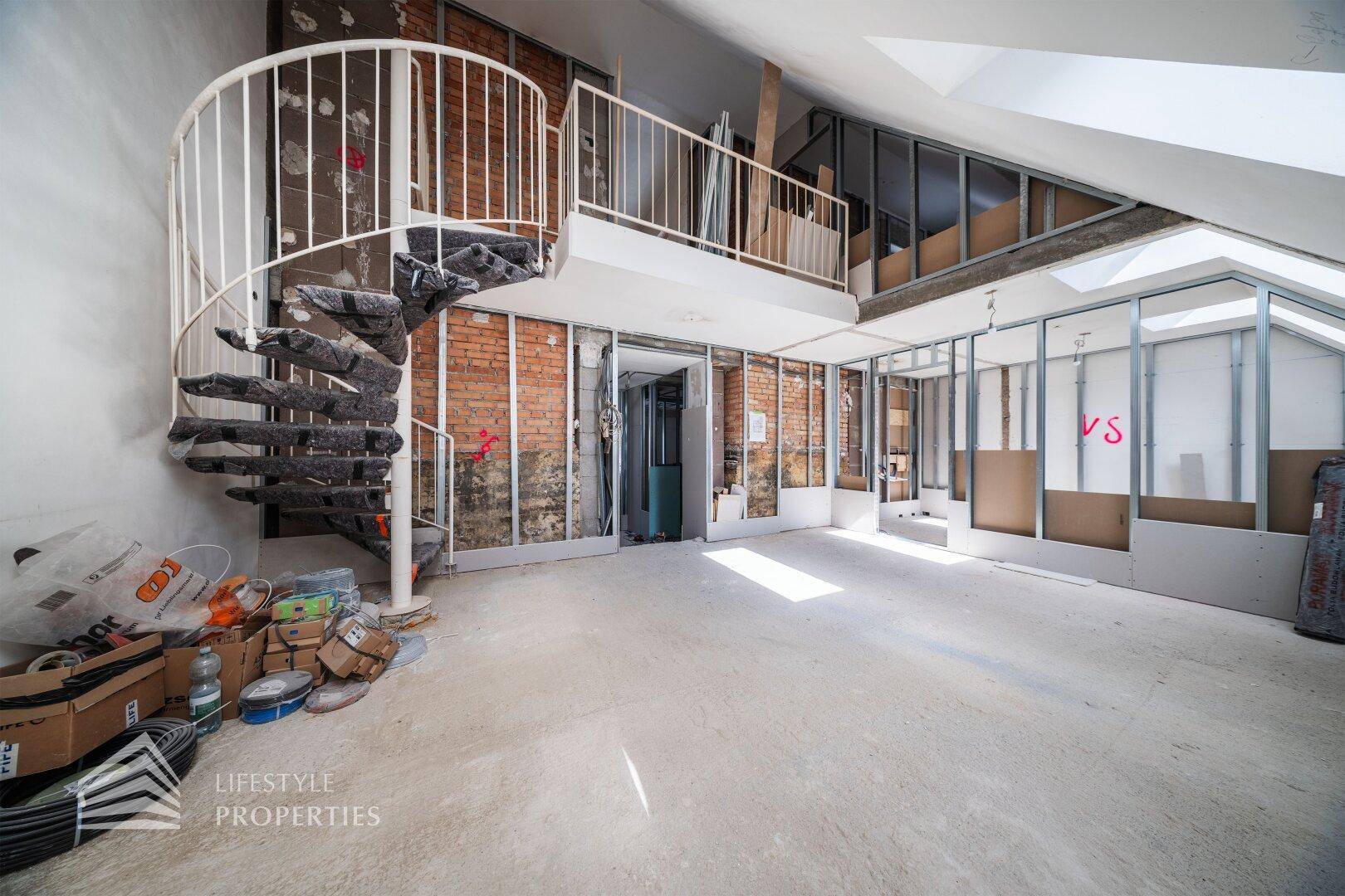 Geräumiges Dachgeschoss im Rohbau mit Wendeltreppe und freigelegten Ziegelwänden.