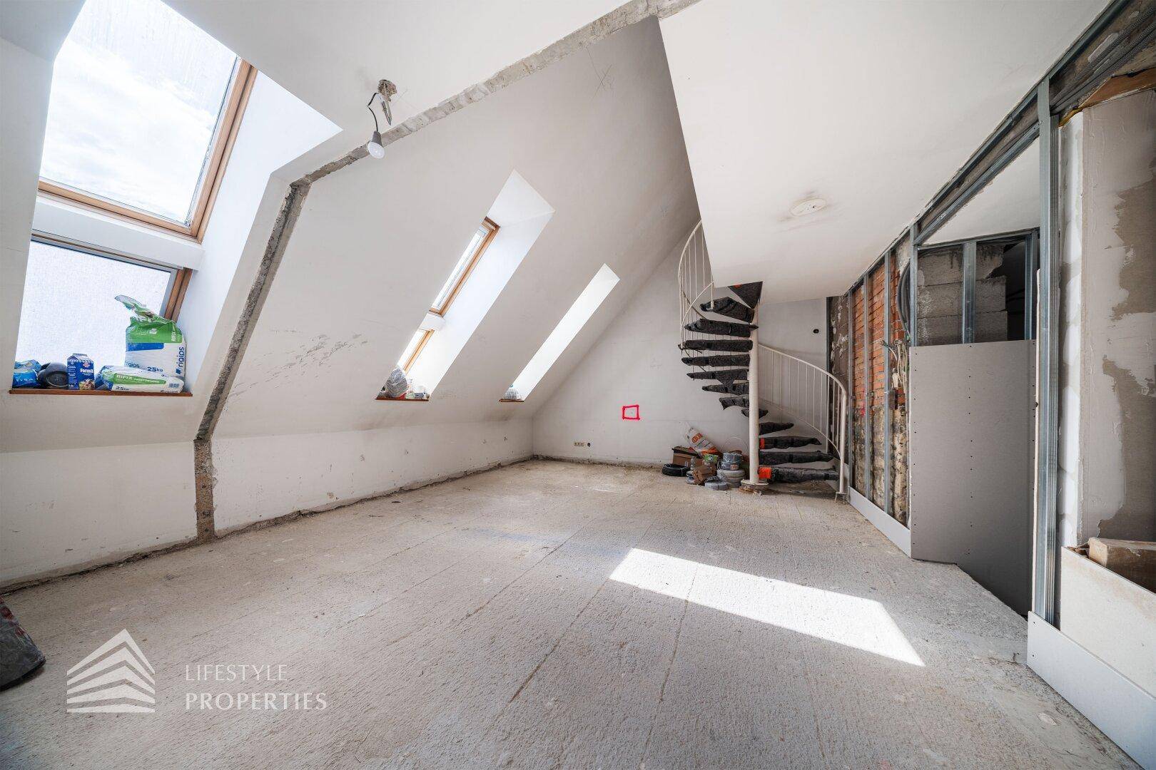 Dachgeschoss im Rohbau mit mehreren Dachfenstern und viel Tageslicht.