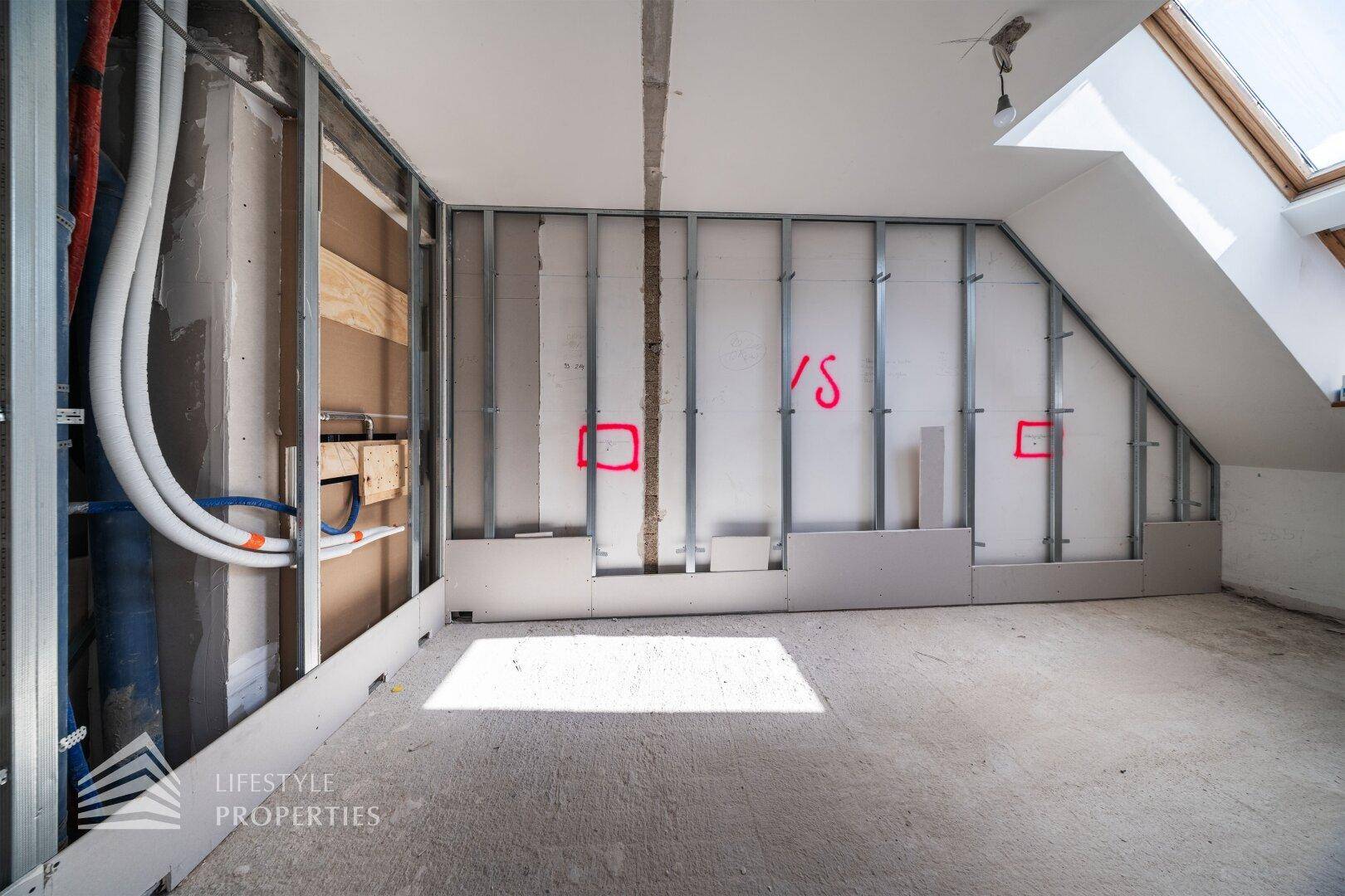 Dachgeschoss im Rohbau mit schrägen Wänden und sichtbaren Trockenbauprofilen.