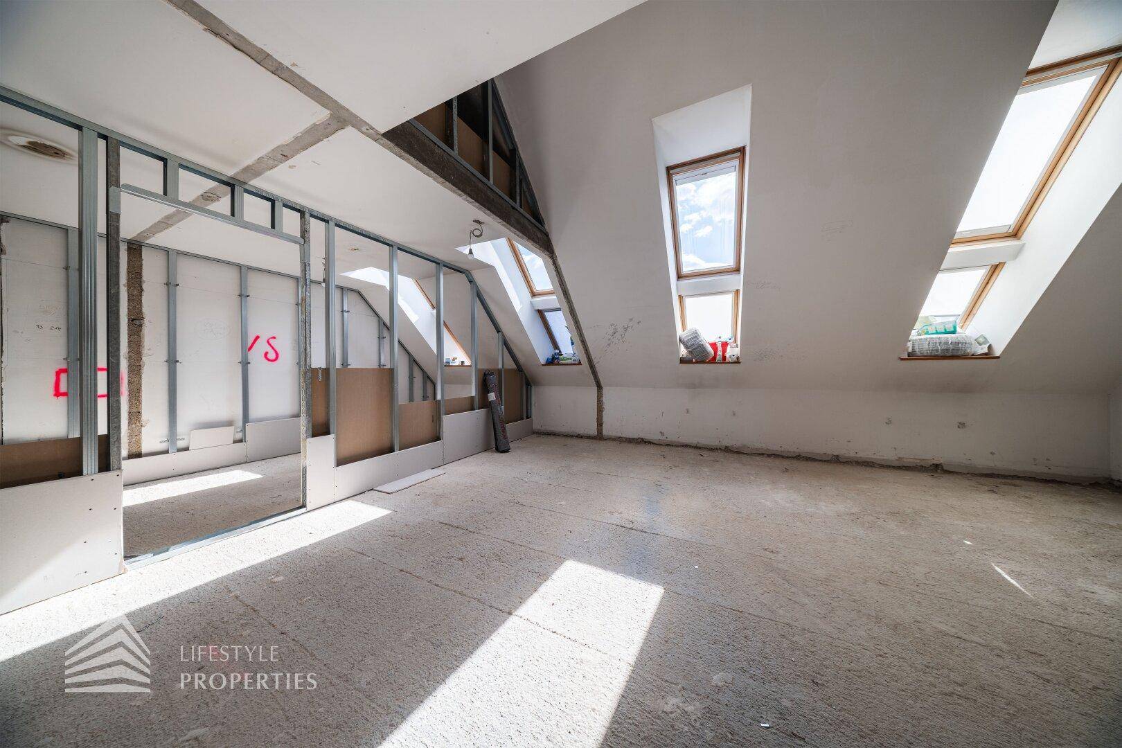 Dachgeschoss im Rohbau mit Dachfenstern und sichtbaren Trockenbauwänden.