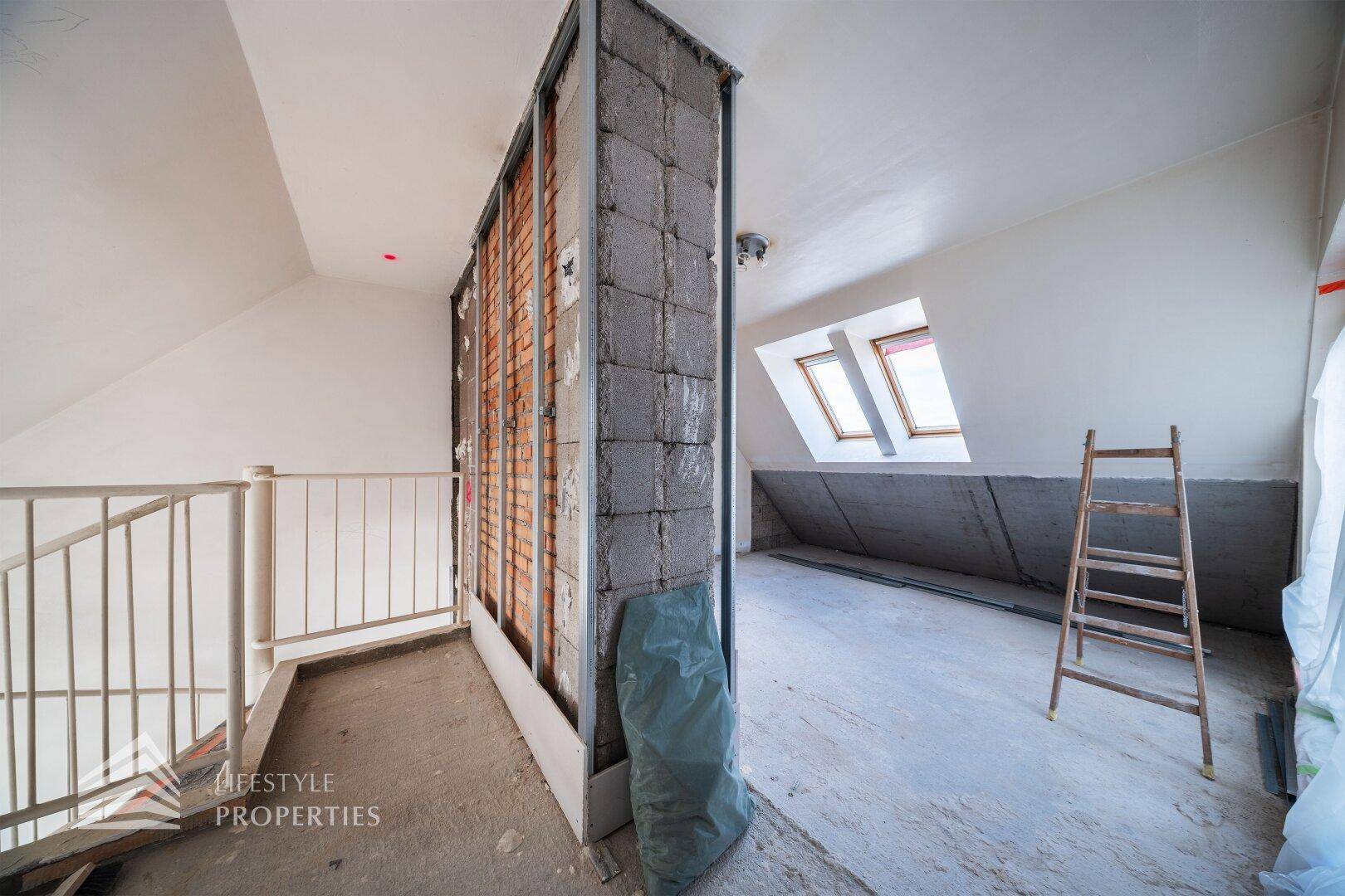 Dachgeschoss im Rohbau mit Treppenaufgang und sichtbaren Konstruktionselementen.