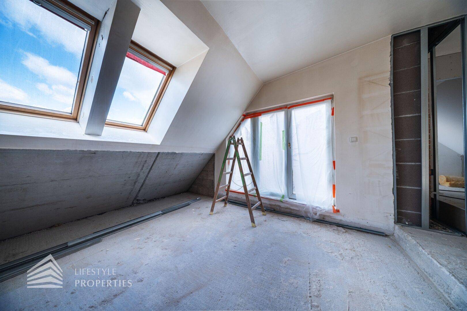 Dachgeschoss im Rohbau mit großen Dachfenstern und viel Tageslicht.