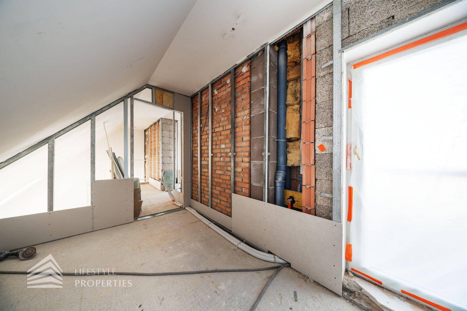 Raum im Rohbau mit sichtbaren Ziegelwänden und vorbereiteten Installationen.