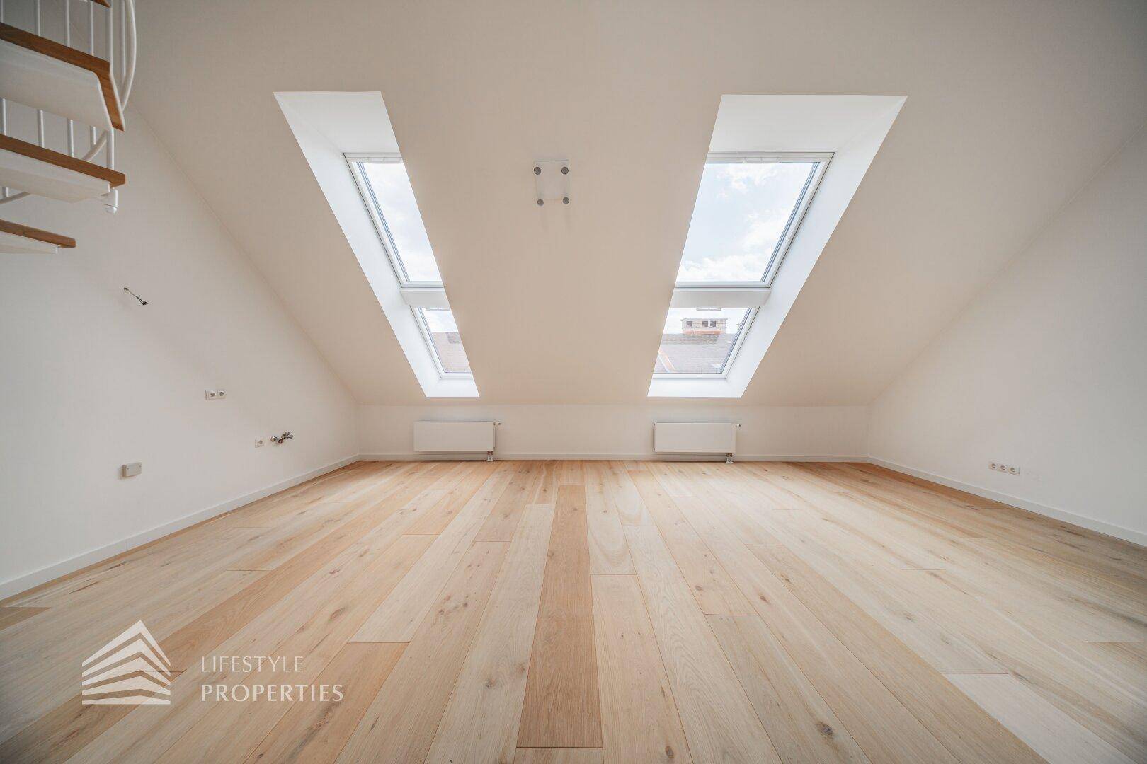 Lichtdurchflutetes Dachzimmer mit zwei großen Dachfenstern und Holzparkettboden.