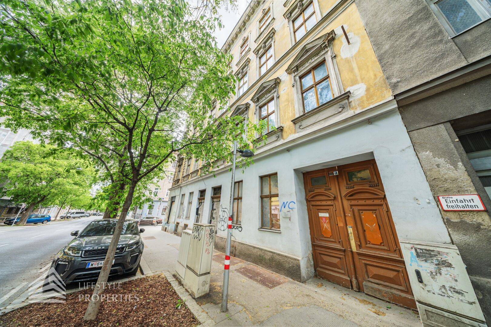 Nahaufnahme einer historischen Gebäudefassade mit einer großen Holztür und einem Baum.