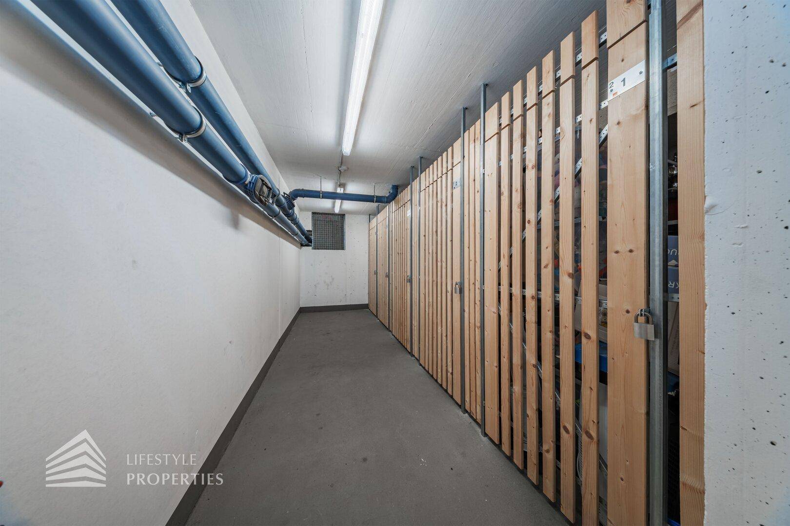 Kellerabteil mit Holzabtrennungen und sichtbaren Leitungen an der Decke für zusätzlichen Stauraum.