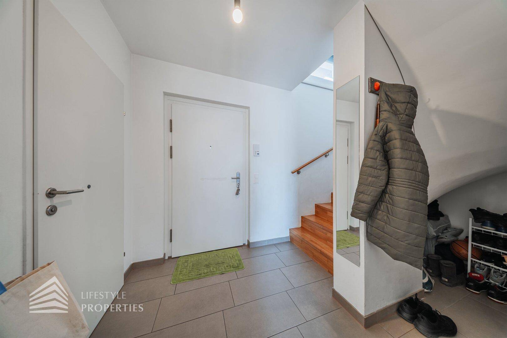 Eingangsbereich mit Fliesenboden, Garderobe und Zugang zur Holztreppe in die oberen Etagen.