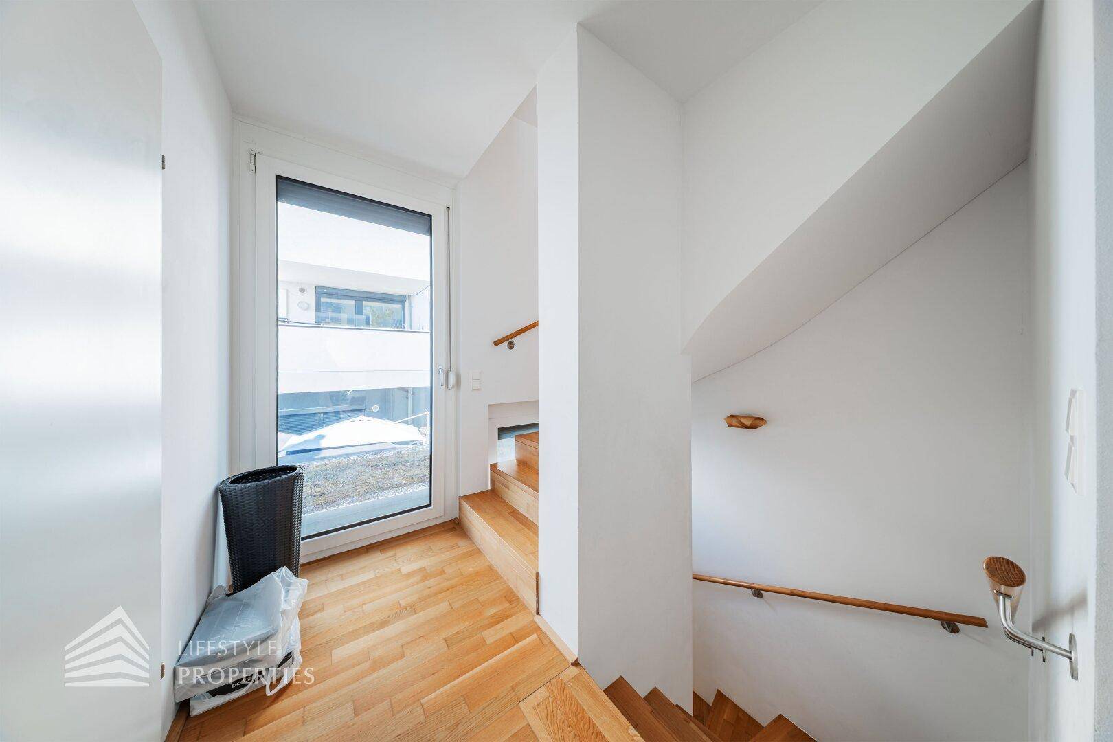 Treppenabsatz mit Holzboden und großem Fenster, das viel Tageslicht in den Bereich bringt.