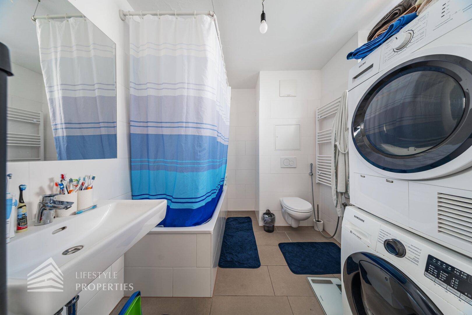 Funktionales Badezimmer mit Badewanne, Toilette, Waschbecken und integrierter Waschmaschine und Trockner.
